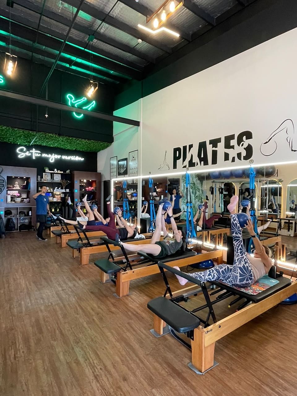 Clase grupal en Reformer: alumnas con las piernas en alto sosteniendo un balón mientras el instructor guía