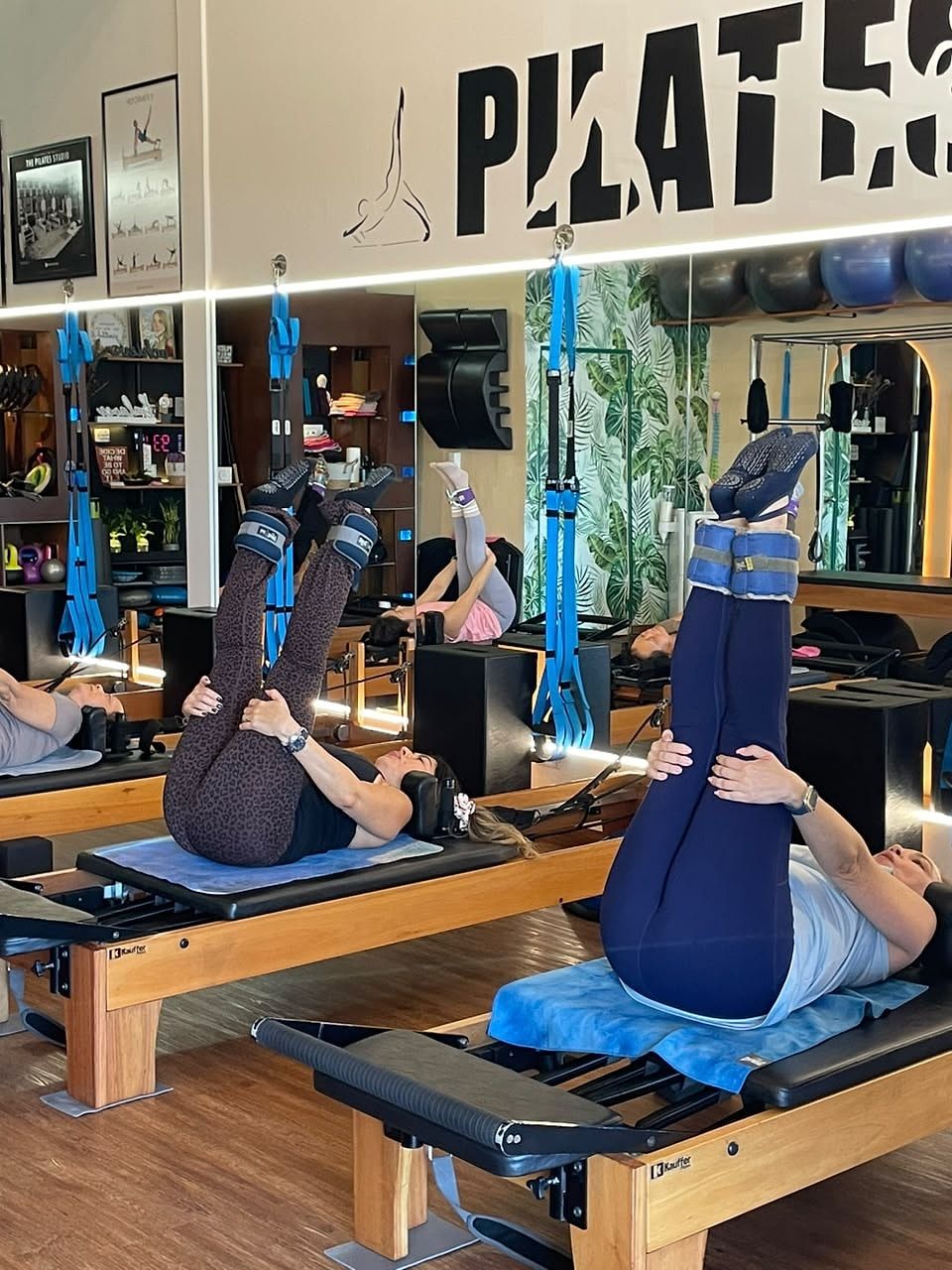 Dos alumnas tumbadas en el Reformer con las piernas en alto y tobilleras de peso