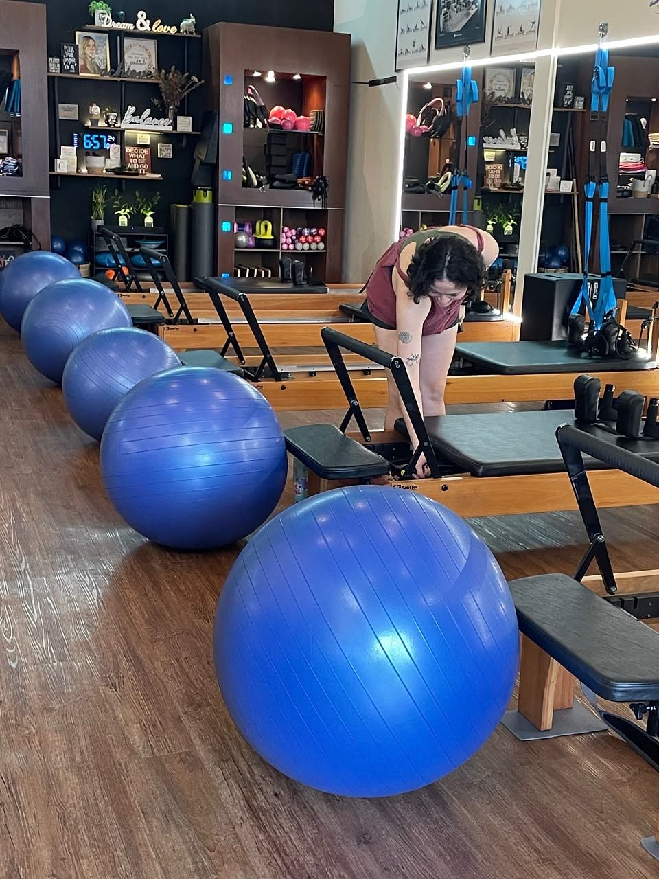 Fila de pelotas fitball azules junto a las máquinas Reformer mientras una alumna prepara su máquina