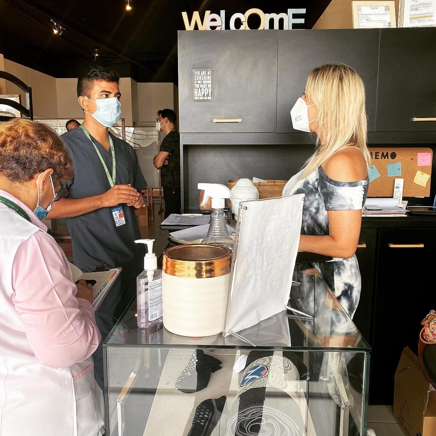 Luzmila con mascarilla conversa en la recepción del estudio con personal sanitario, junto a gel desinfectante