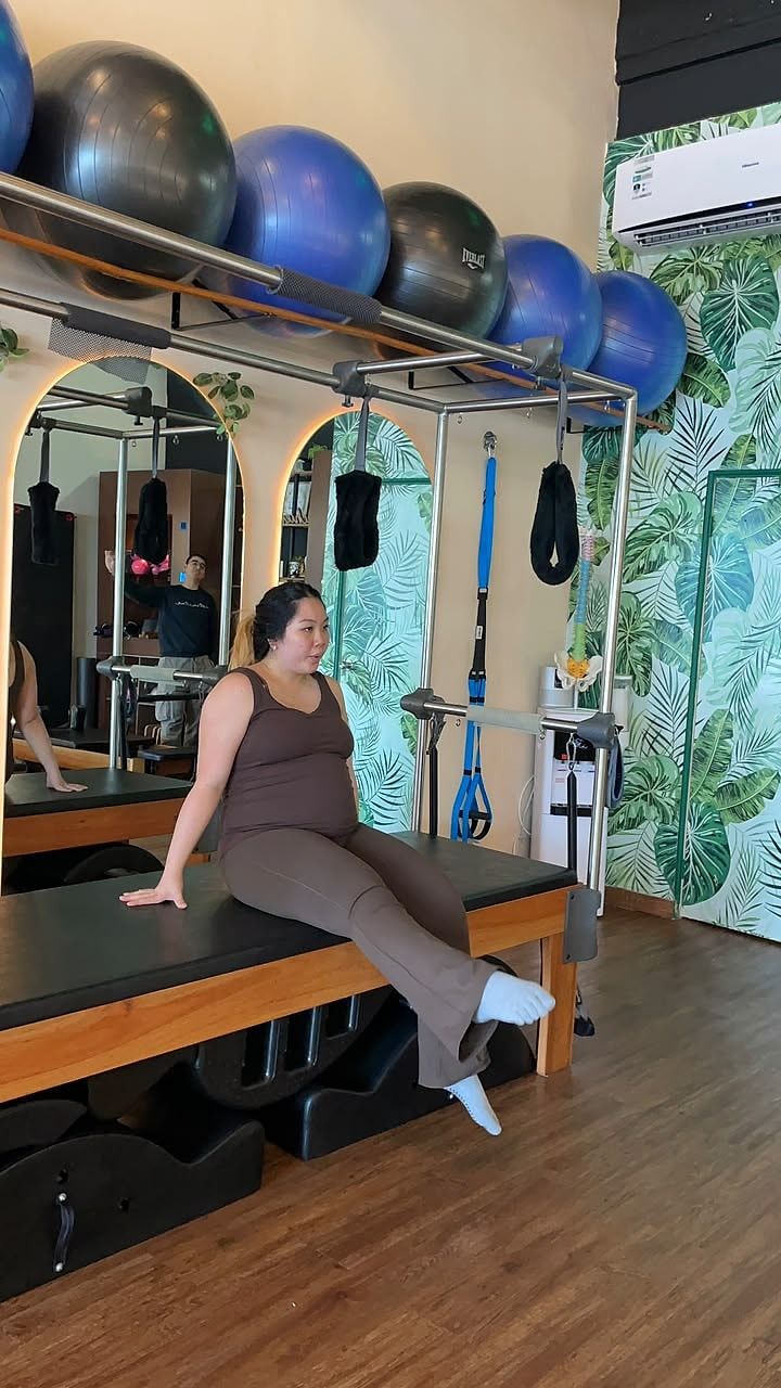Alumna embarazada sentada en la máquina Cadillac durante una sesión de Pilates prenatal